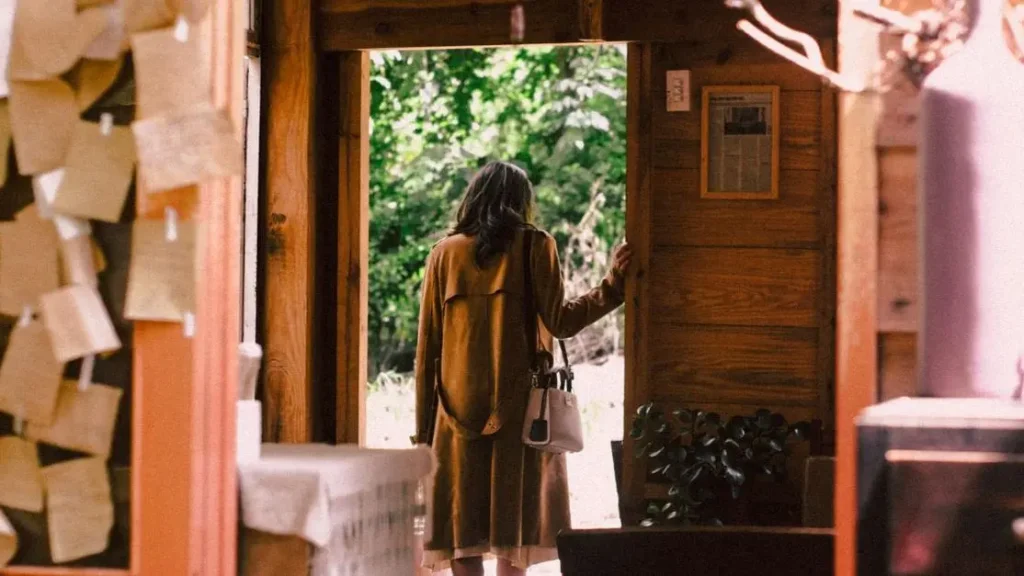 Woman steps from a cozy cabin into sunlight, symbolizing how to enter the kingdom of God